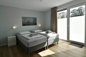 Een moderne slaapkamer met een bed, nachtkastjes, een kunstwerk aan de muur en een schuifdeur van glas naar buiten.
