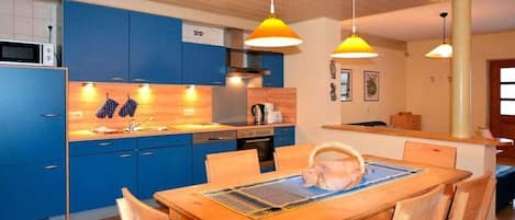 Una cocina moderna con armarios azules, una mesa de comedor de madera e iluminación colgante.