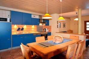 Une cuisine moderne avec des meubles bleus, une table à manger en bois et des luminaires suspendus.