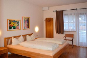 Une chambre à coucher avec un lit double, deux tableaux accrochés au mur, une armoire en bois, une chaise et une fenêtre avec des rideaux.