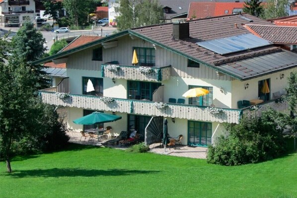 Un bâtiment à deux étages doté d’un balcon, d’un espace extérieur aménagé pour s’asseoir et d’un panneau solaire sur le toit.