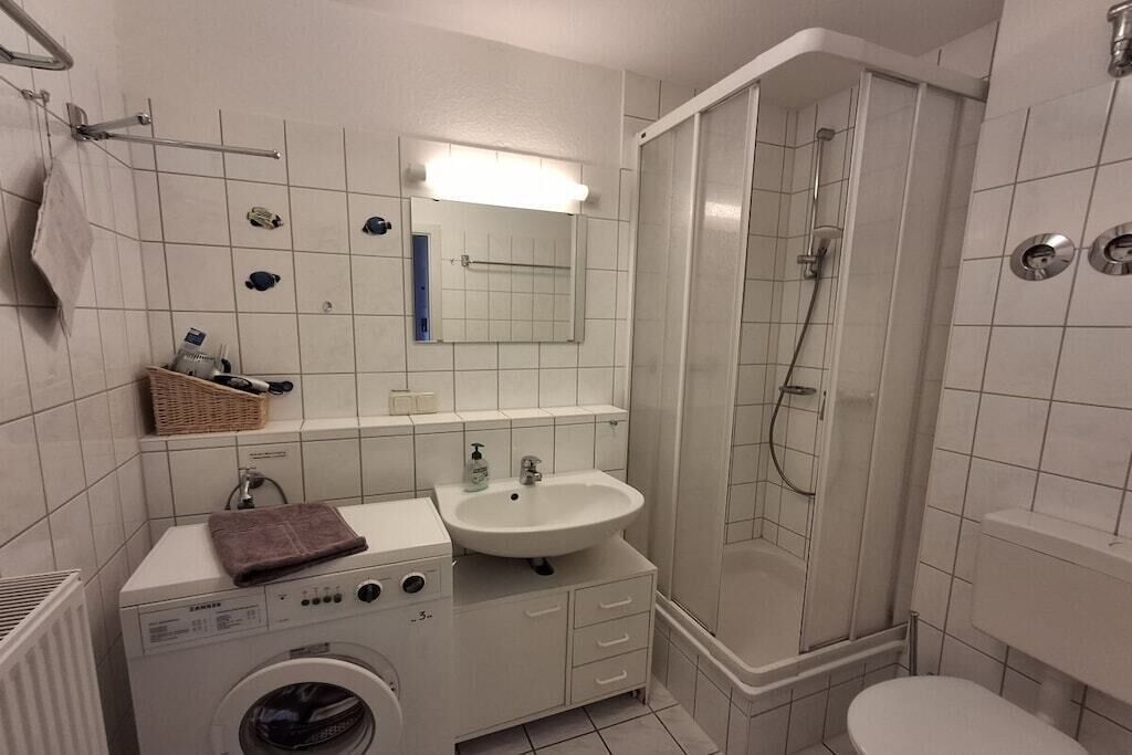 A compact bathroom with a washing machine, a sink, a mirror, and a shower enclosure.