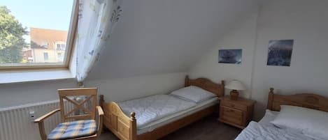 A bedroom with a single bed, a chair, a bedside table with a lamp, and a window with curtains.