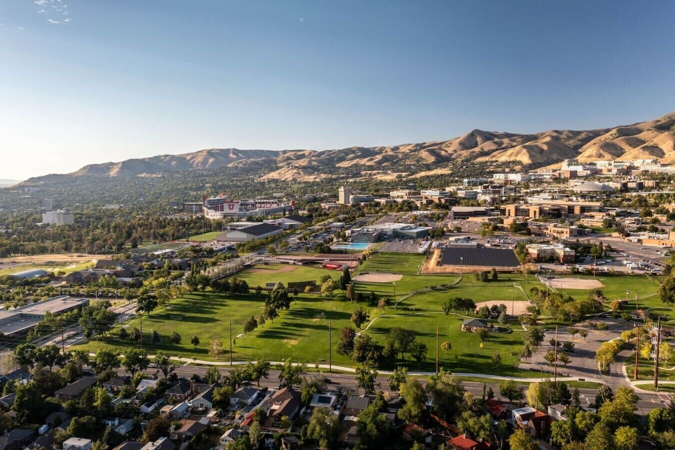 A residential area with houses, a large building complex, and a hilly landscape in the background.