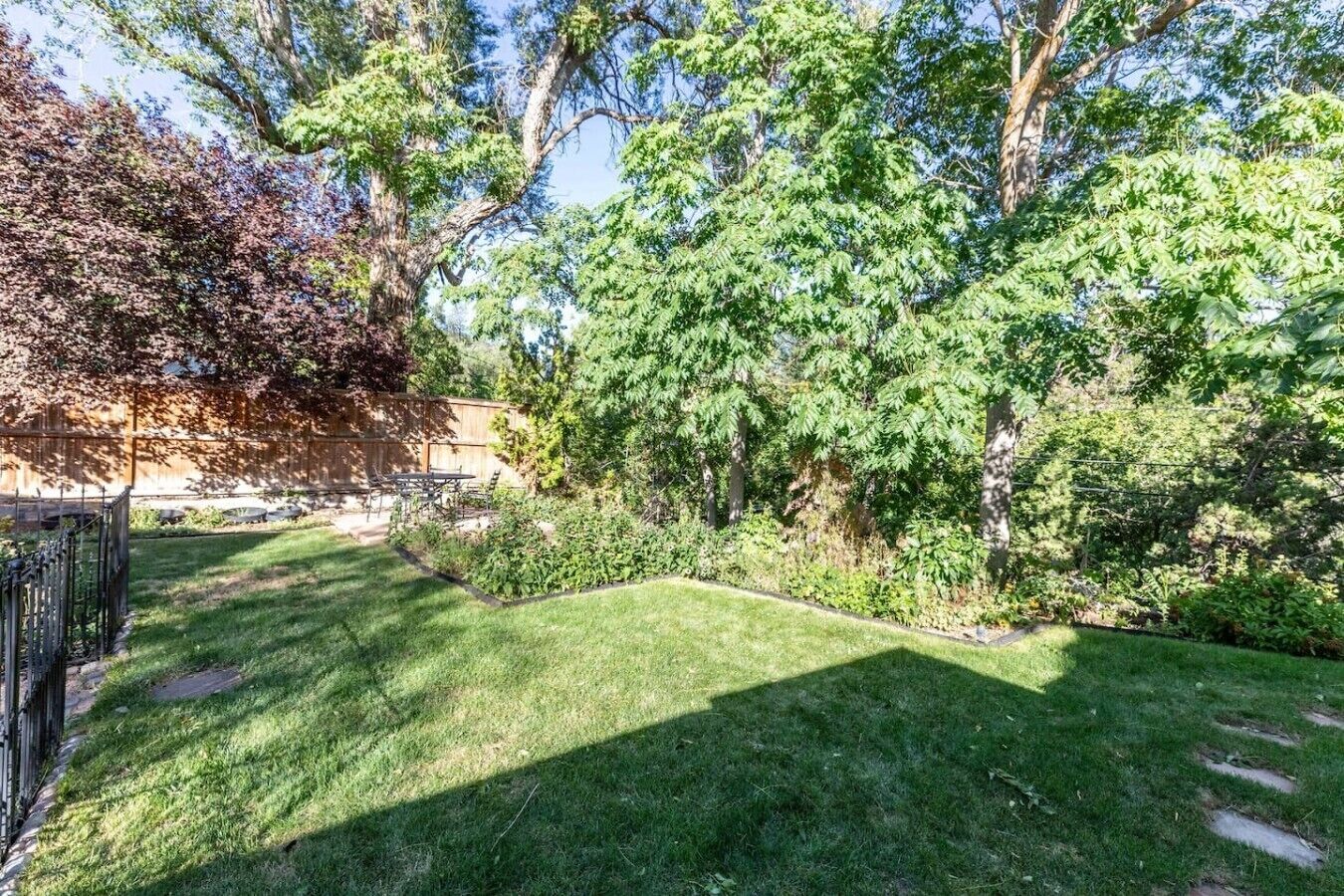 A well-maintained backyard with a lawn, a wooden fence, and a variety of trees.