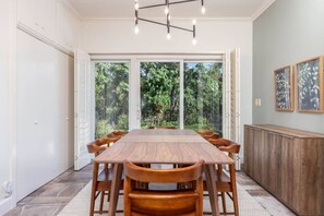 A dining area with a large wooden table and chairs, a modern light fixture, and a view of greenery through large windows. - Red Butte River Gem-Close to the U, Downtown & Mtn (Salt Lake City)