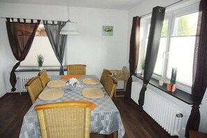 A dining area with a table set for four, surrounded by chairs, a radiator, and a window with curtains. - Holiday home in Hinte with swimming pool (Hinte)