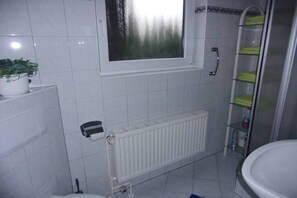 Ein Badezimmer mit Toilette, Heizkörper, Ablagefläche für Handtücher und einem Fenster.