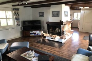 Sala de estar com lareira, televisão e área de estar com cadeiras azuis.