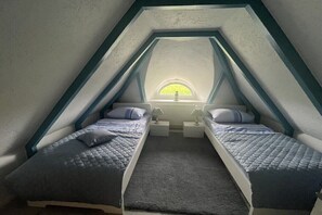 Quarto de sótão triangular com duas camas, um claraboia e uma pequena janela.
