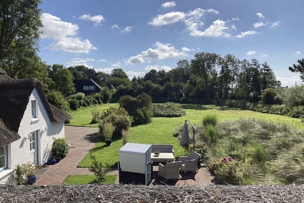Une maison avec un toit de chaume, un chemin pavé et un jardin verdoyant agrémenté de meubles d’extérieur.