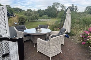 Une terrasse extérieure avec des meubles en osier, une table ronde et un parasol blanc.