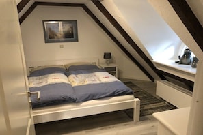 Une chambre avec un plafond en pente, un lit avec un matelas bleu, une table de chevet avec une lampe et une fenêtre donnant sur l’extérieur.