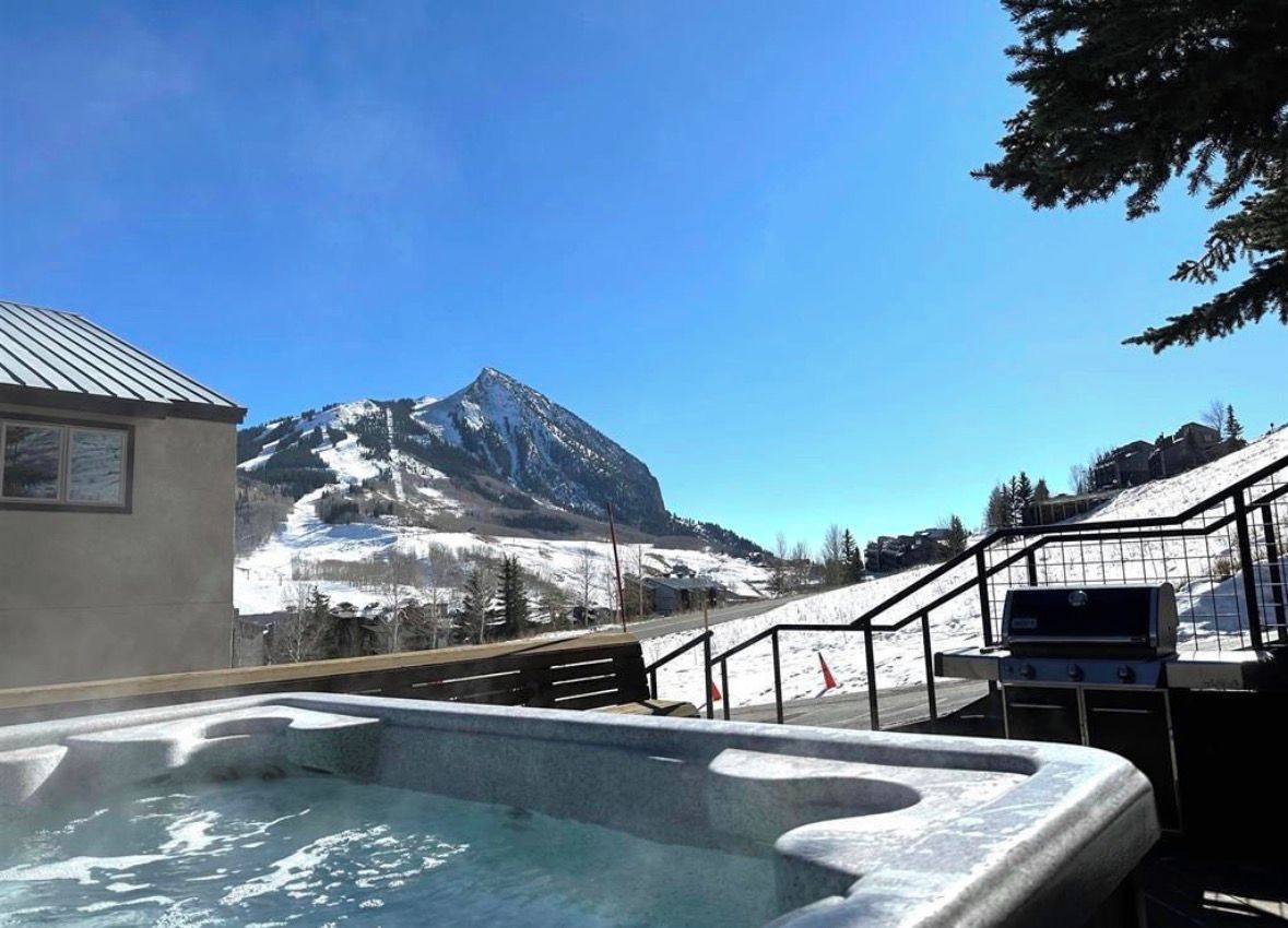 A hot tub with a mountain view, a barbecue grill, and a staircase leading to a snowy area.