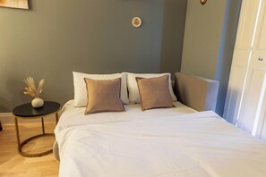 A bedroom with a bed, pillows, a small round table with a vase, and a door. - Central London 1BR | Trafalgar Square | Sleeps 4 (London)