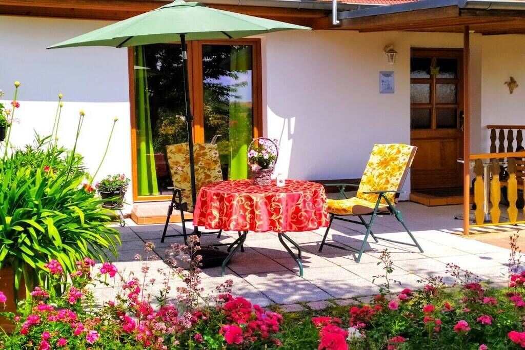 An outdoor patio with a table and chairs, surrounded by potted plants and flowers.