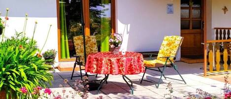 An outdoor patio with a table and chairs, surrounded by potted plants and flowers.