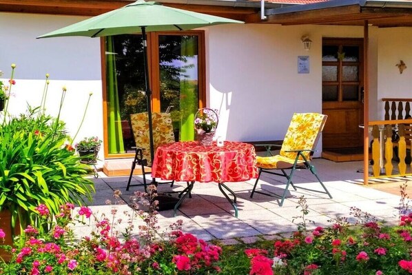 Un patio al aire libre con una mesa y sillas, rodeado de plantas y flores en macetas.