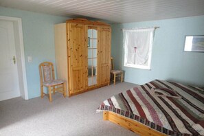 A bedroom with a bed, a wooden wardrobe, a chair, and a window with curtains.