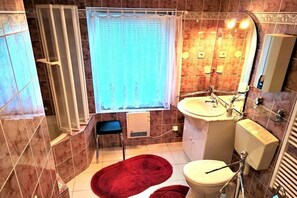 Un baño con ducha, inodoro, lavamanos y una ventana con cortinas.