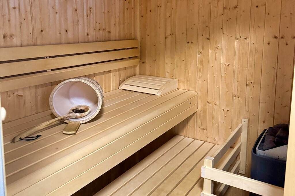 A sauna room with wooden benches, a bench heater, and a trash bin.