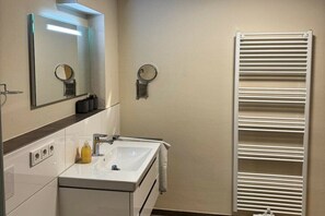 Une salle de bain avec un lavabo blanc, un miroir, un porte-serviettes et une serviette blanche accrochée au mur.
