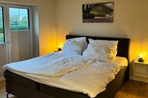 Un lit bien fait, avec du linge de lit blanc, une tête de lit sombre et deux lampes de chevet.