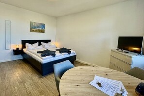 Ein Schlafzimmer mit einem Bett, Nachttischen, einem Fernseher, einem Schreibtisch mit Papieren und einem Bild an der Wand.