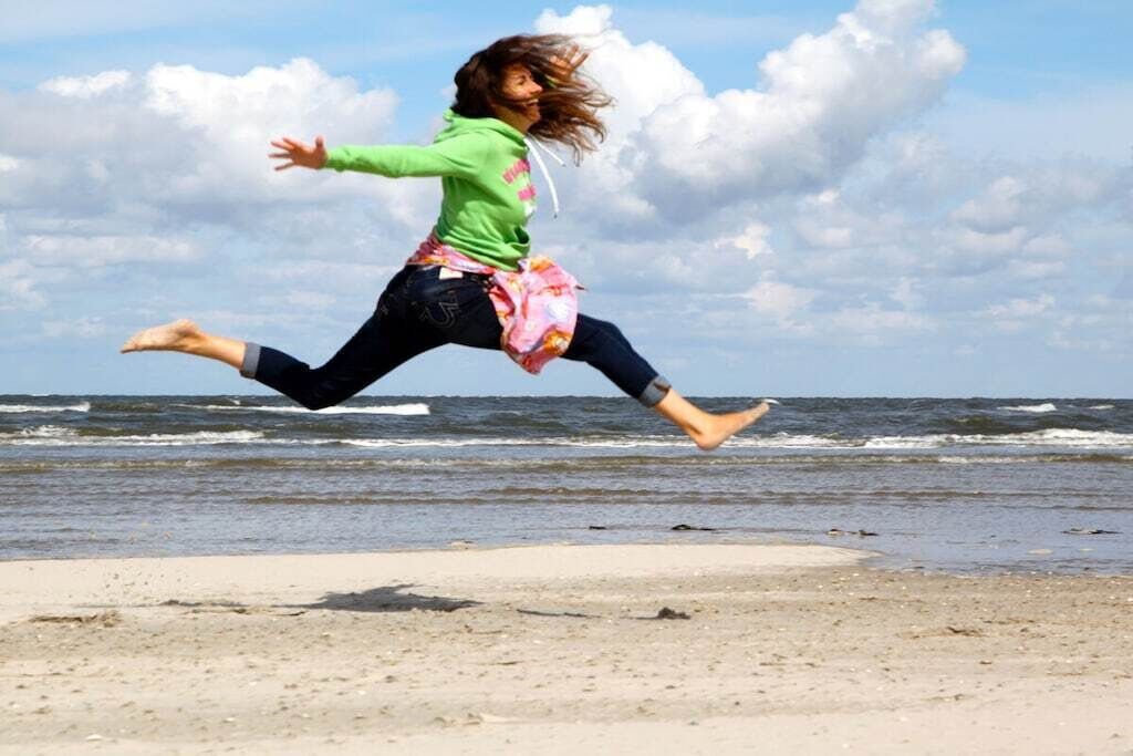 A person jumping on a beach with waves in the background.