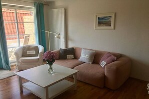 Ein Wohnzimmer mit einem weißen Couchtisch, einem beigen Sofa mit dekorativen Kissen, einer Stehlampe und einem gerahmten Bild an der Wand.