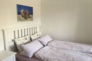 Ein Einzelbett mit weißem Kopfteil, zwei Kissen mit Blumenmuster und ein Strandbild über dem Bett.