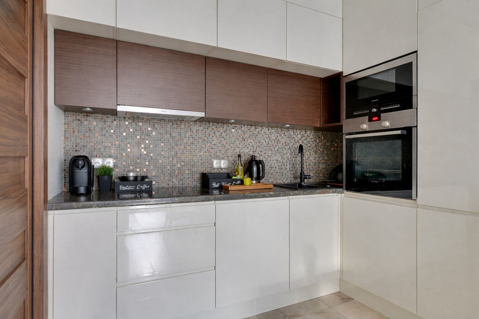 Eine moderne Küche mit weißen Schränken, einer gefliesten Rückwand und Edelstahlgeräten, darunter ein Backofen und eine Kaffeemaschine.