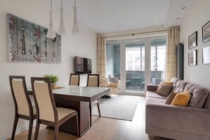 A modern living room with a sofa, a dining table with chairs, a TV, and a large window with curtains. - Old Town Gdansk with Parking - Tandeta 1 (Gdańsk)