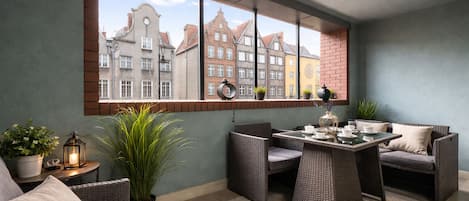 Uma varanda com mobiliário de vime, uma mesa posta para refeições e vista para edifícios.