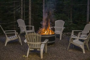 Ein Lagerfeuer mit vier Adirondack-Stühlen, die darum angeordnet sind.