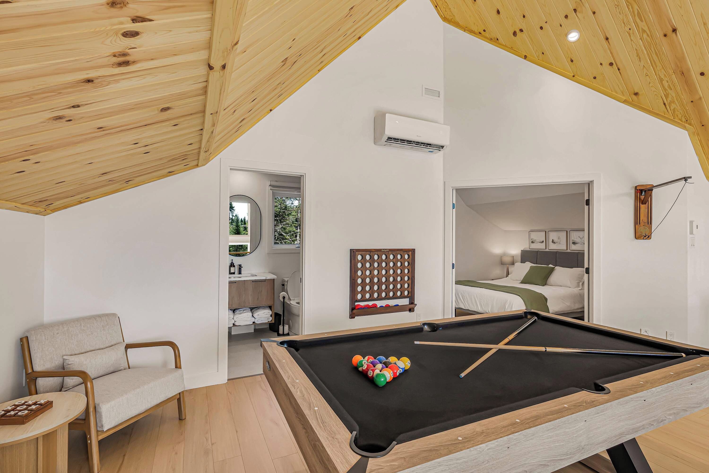 A modern room with a pool table, a chair, a bed, and a bathroom visible through an open door.