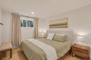 Ein Schlafzimmer mit einem Bett, Nachttischen, einem Fenster mit Vorhängen und einem Bild an der Wand.