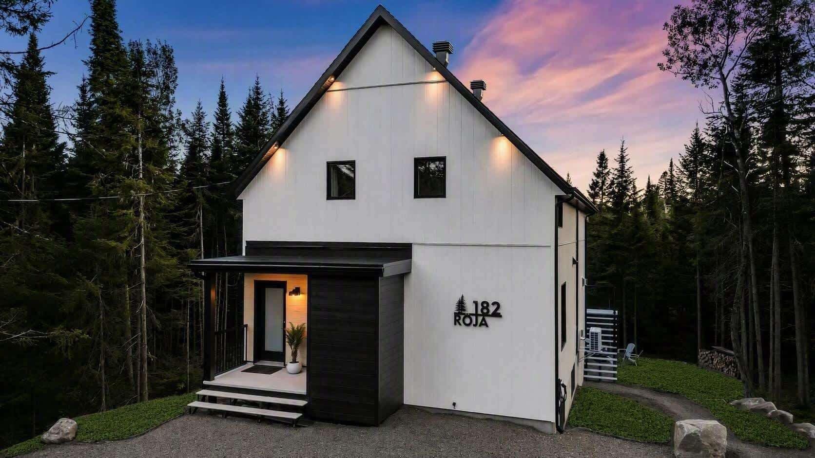 Ein modernes, zweistöckiges Haus mit weißer Fassade, Hausnummer 182, umgeben von einem bewaldeten Gebiet.