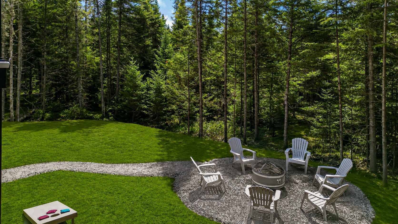 A circular outdoor seating area with Adirondack chairs, a fire pit, and a gravel path.
