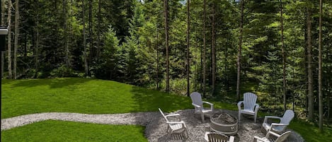 A circular outdoor seating area with Adirondack chairs, a fire pit, and a gravel path.