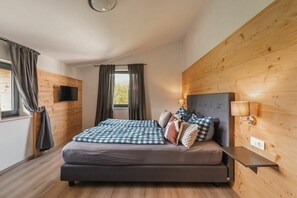 A bedroom with a bed, curtains, a wall-mounted TV, and a bedside table. - Cabin in Inzell with swimming pool (Inzell)