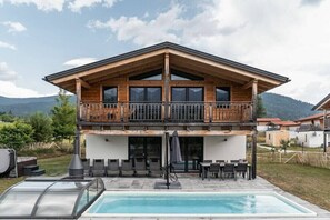 A two-story wooden chalet with a balcony, a swimming pool, and outdoor seating. - Cabin in Inzell with swimming pool (Inzell)