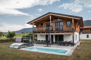 Ein zweistöckiges Holzhaus mit Balkon, Schwimmbecken und einer Terrassenfläche.