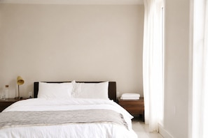 A hotel room with a bed, bedside tables, a lamp, and a window with curtains.