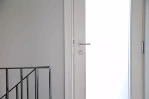 A white door with a silver handle and a keyhole, a metal railing to the left, and a plain wall.