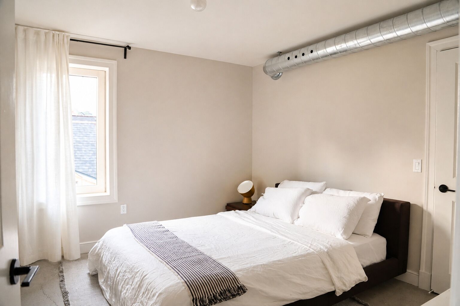 A bedroom with a bed, a nightstand, a lamp, and a window with curtains.