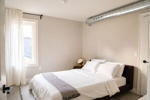 A bedroom with a bed, a nightstand, a lamp, and a window with curtains.