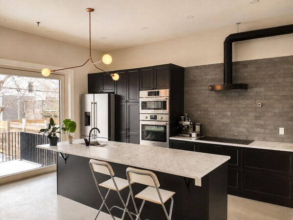 A modern kitchen with a central island, black cabinetry, stainless steel appliances, and a large window.