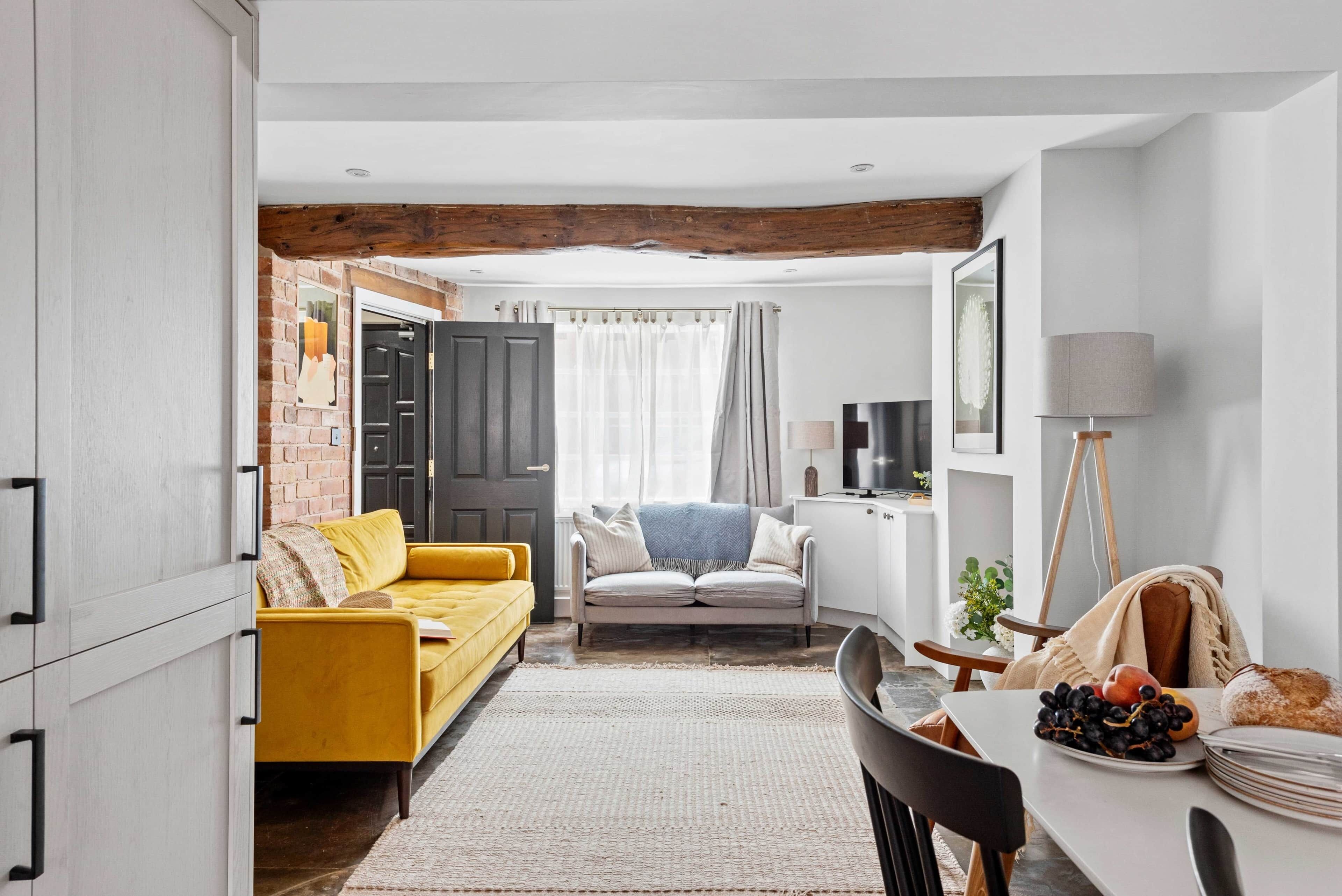 Una sala de estar moderna con un sofá amarillo, un sofá gris y una mesa de comedor con platos de fruta.