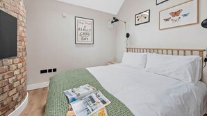 Una camera da letto con parete in mattoni, un letto con biancheria bianca, una coperta verde e una citazione incorniciata appesa al muro.